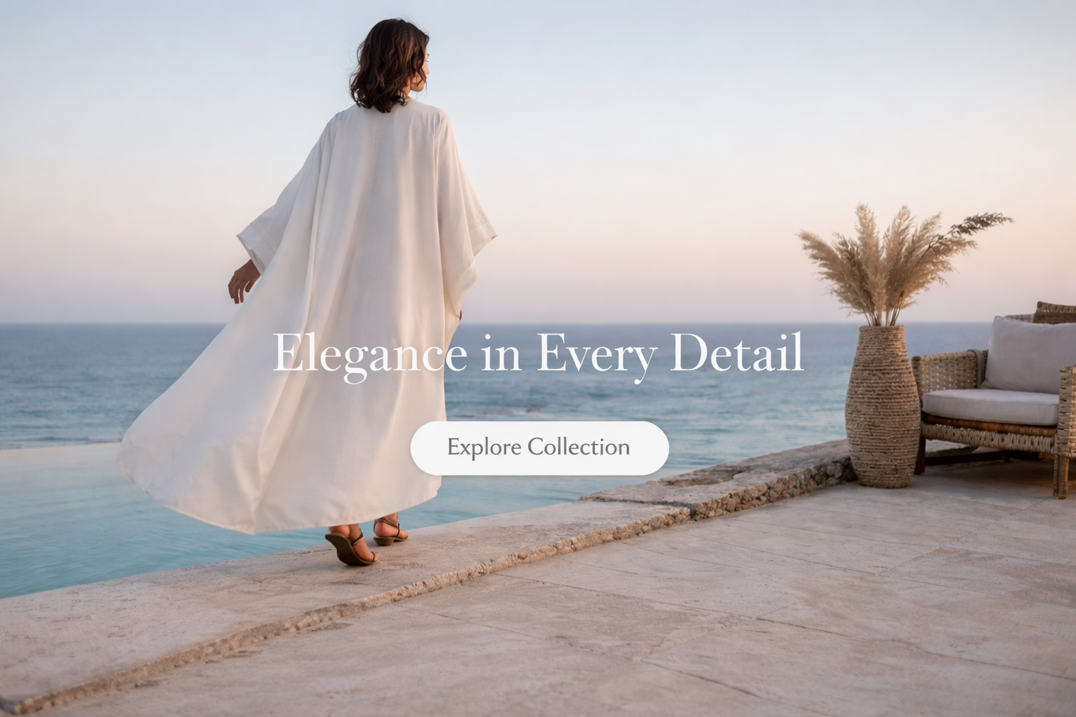 Woman in a white abaya dress standing by the ocean with text overlay 'Elegance in Every Detail' and 'Explore Collection'.
